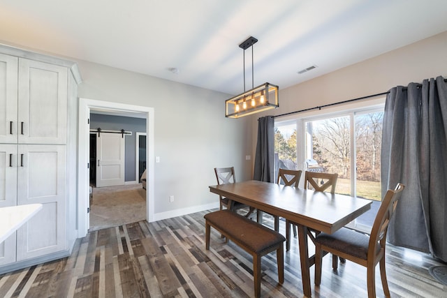 dining area featuring dark wood-style floors, a notable chandelier, visible vents, a barn door, and baseboards