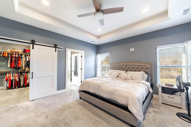 bedroom with carpet floors, a tray ceiling, a walk in closet, visible vents, and a barn door