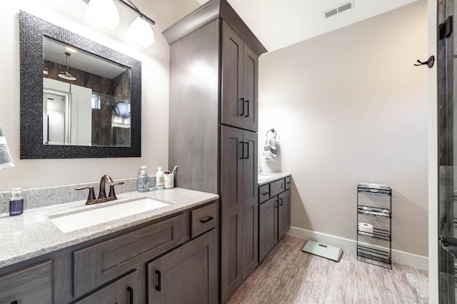 bathroom featuring wood finished floors, two vanities, a sink, visible vents, and baseboards