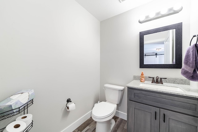 half bath with vanity, wood finished floors, toilet, and baseboards