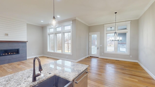 kitchen with stainless steel dishwasher, ornamental molding, a fireplace, and light wood-style flooring