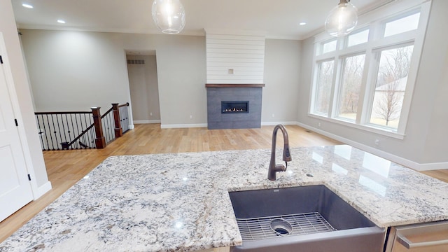 kitchen with a fireplace, light wood-style flooring, ornamental molding, a sink, and baseboards