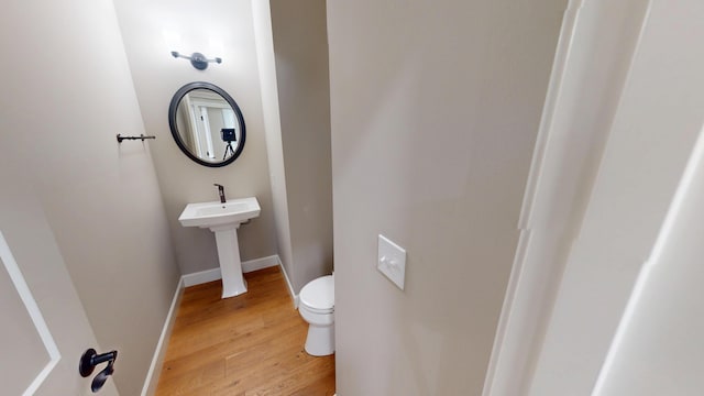 half bathroom with toilet, a sink, baseboards, and wood finished floors