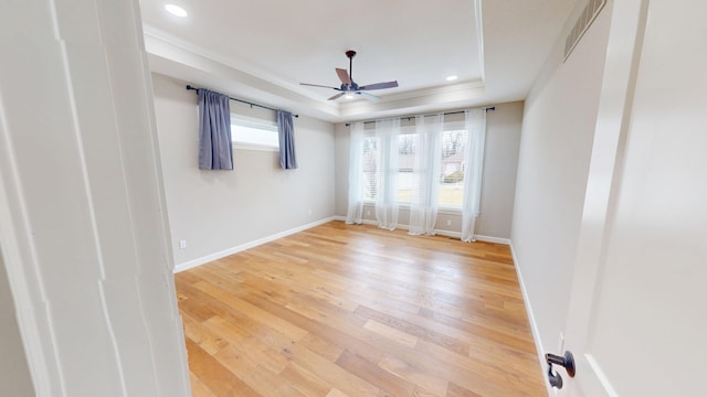 spare room with a raised ceiling, visible vents, ceiling fan, light wood-type flooring, and baseboards