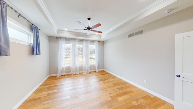 unfurnished room with a tray ceiling, light wood-type flooring, visible vents, and a healthy amount of sunlight