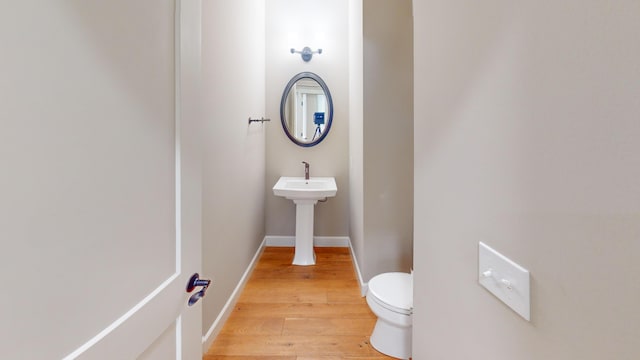 half bath with wood finished floors, toilet, and baseboards