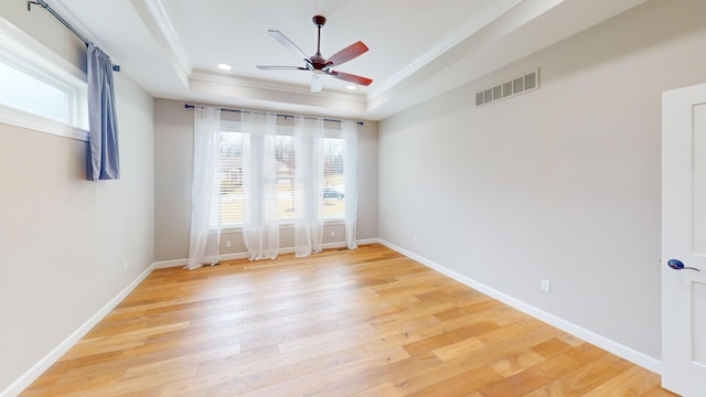 unfurnished room with light wood-style flooring, visible vents, baseboards, ornamental molding, and a raised ceiling