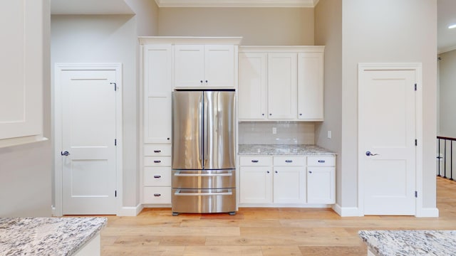 kitchen featuring light wood finished floors, light stone counters, freestanding refrigerator, white cabinetry, and backsplash