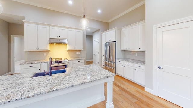 kitchen featuring light wood finished floors, white cabinets, stainless steel appliances, under cabinet range hood, and a sink