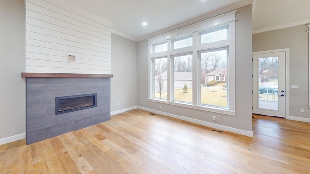 unfurnished living room featuring baseboards, visible vents, a tile fireplace, light wood-style flooring, and crown molding