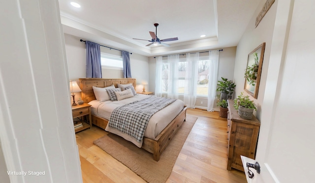 bedroom featuring a tray ceiling, multiple windows, light wood-style flooring, and recessed lighting