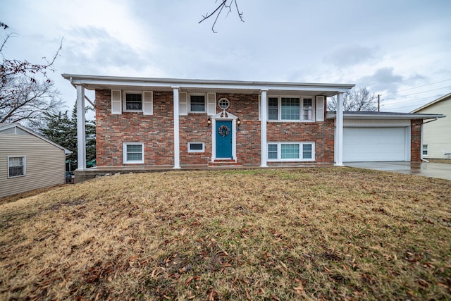 bi-level home featuring a garage, driveway, brick siding, and a front yard