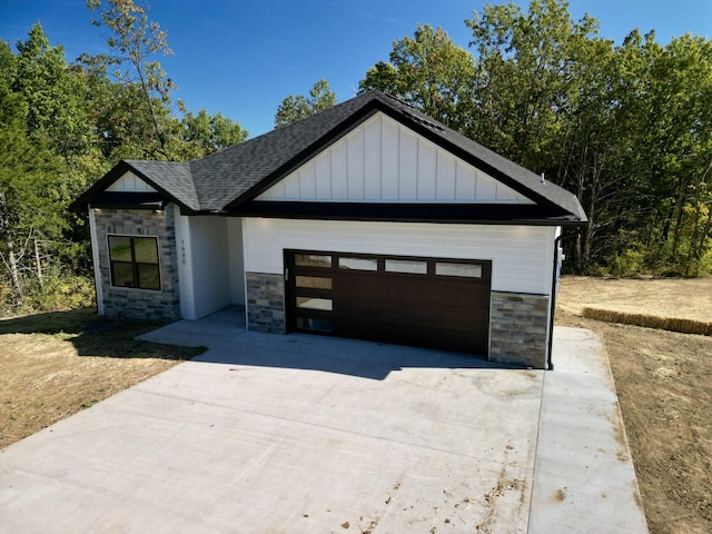 view of front of house featuring a shingled roof, board and batten siding, a garage, stone siding, and driveway