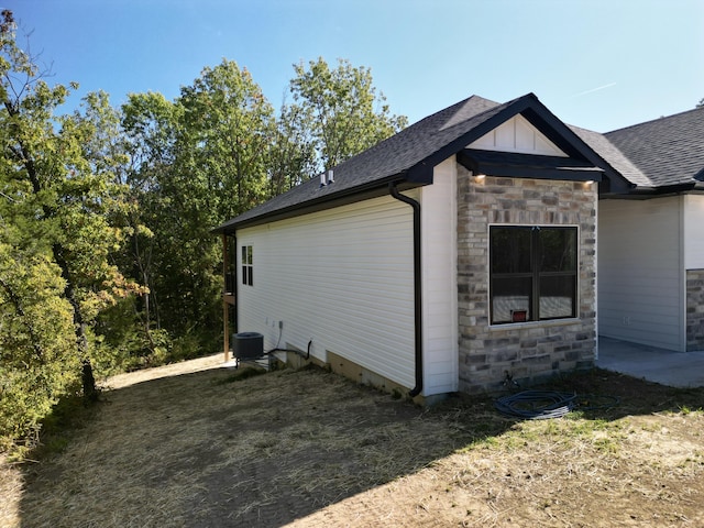 view of home's exterior featuring board and batten siding, stone siding, a shingled roof, and central AC unit