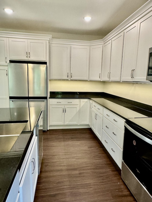 kitchen featuring appliances with stainless steel finishes, dark countertops, white cabinetry, and dark wood finished floors