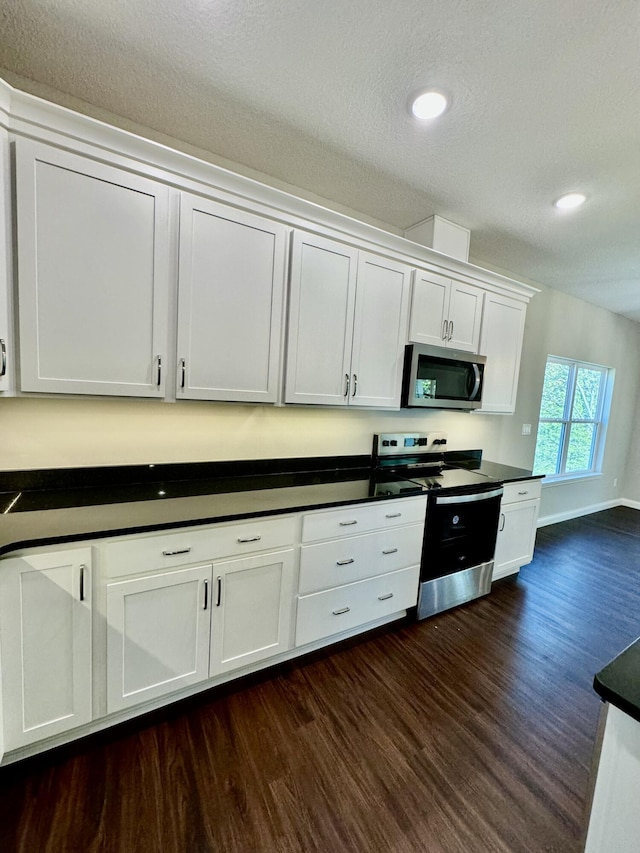 kitchen featuring dark countertops, dark wood-style floors, appliances with stainless steel finishes, white cabinetry, and recessed lighting