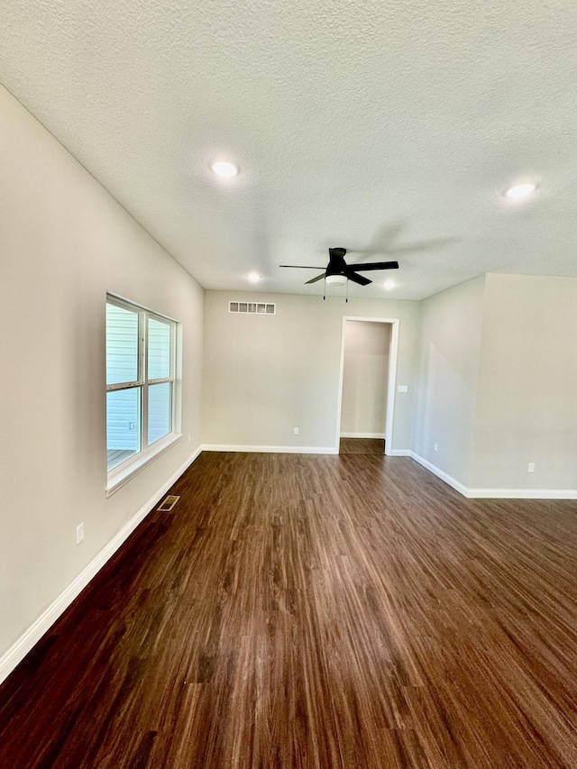 spare room featuring baseboards, visible vents, dark wood finished floors, a ceiling fan, and a textured ceiling