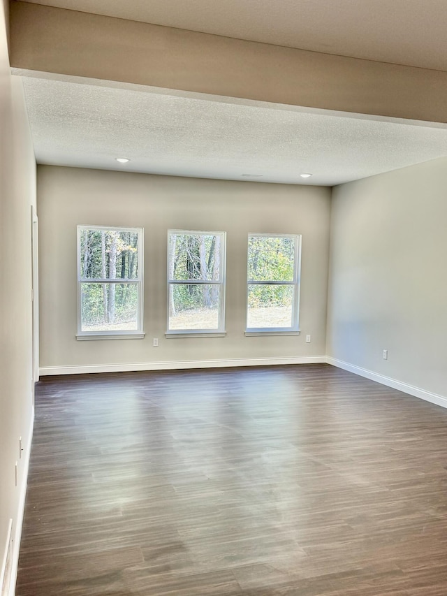 unfurnished room with a textured ceiling, baseboards, wood finished floors, and a healthy amount of sunlight