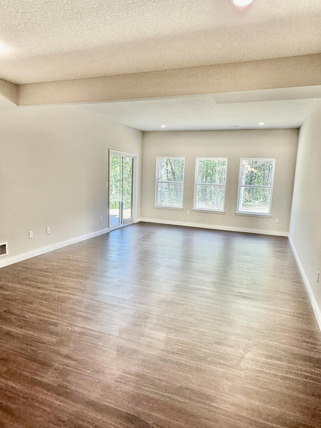 spare room with dark wood-style flooring, visible vents, a textured ceiling, and baseboards