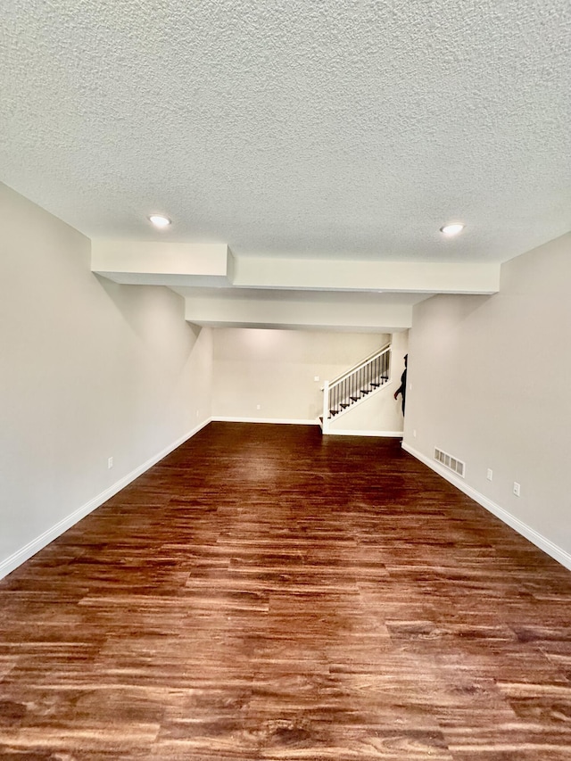 finished below grade area with a textured ceiling, stairs, baseboards, and wood finished floors