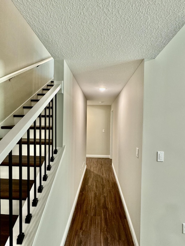 hallway with stairs, a textured ceiling, baseboards, and wood finished floors