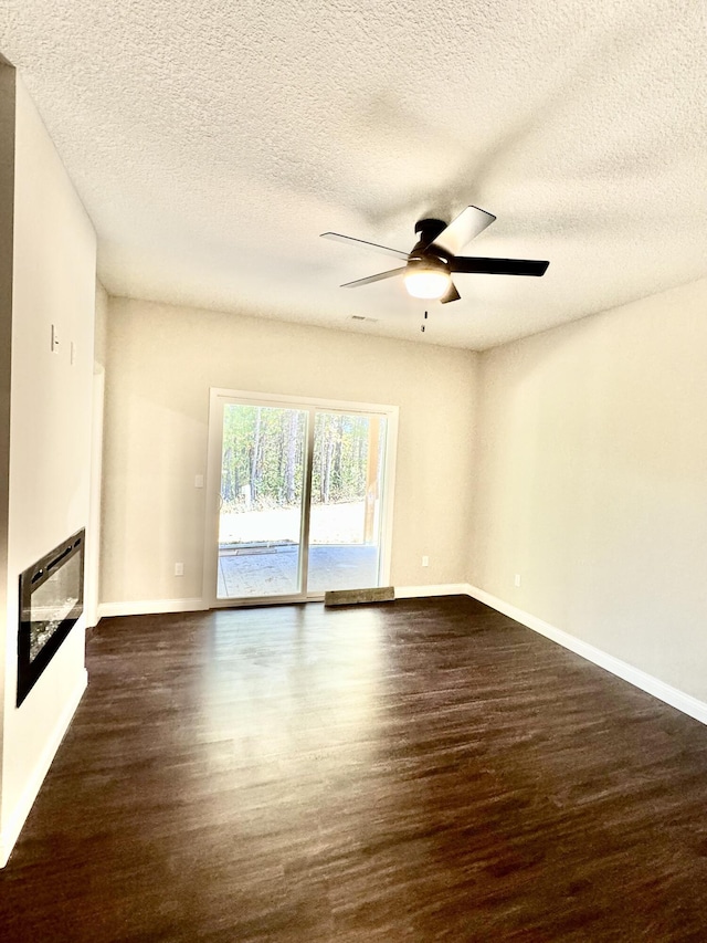 unfurnished living room featuring dark wood-style floors, a glass covered fireplace, baseboards, and a ceiling fan