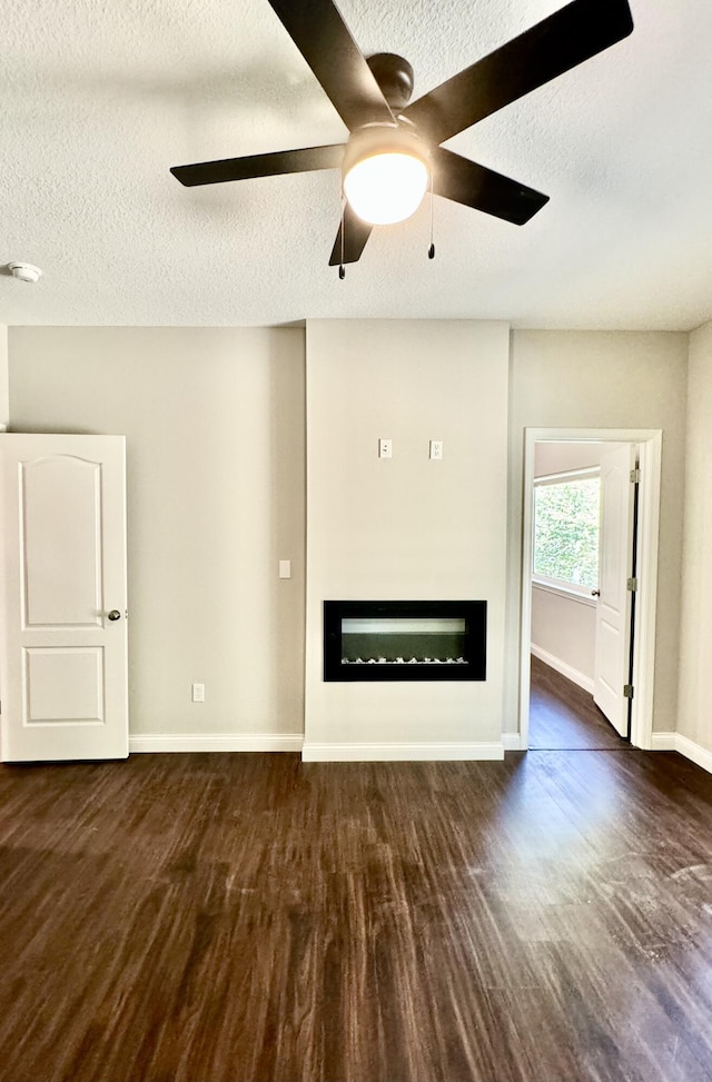 unfurnished living room with a glass covered fireplace, ceiling fan, baseboards, and wood finished floors