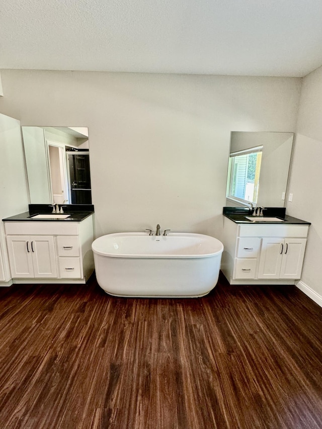 bathroom with a freestanding bath, a stall shower, two vanities, and wood finished floors