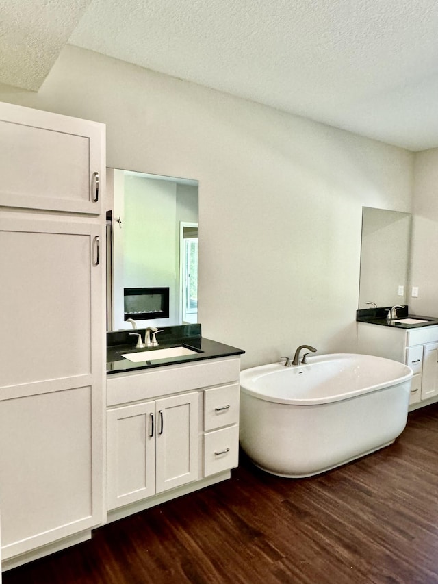 full bath featuring wood finished floors, two vanities, a soaking tub, and a sink