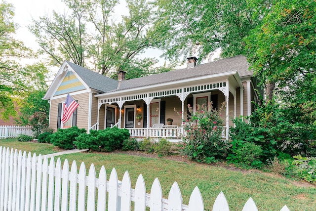 victorian home with a chimney, a shingled roof, covered porch, fence, and a front lawn