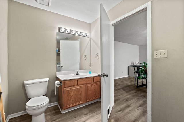 bathroom featuring toilet, baseboards, wood finished floors, and vanity