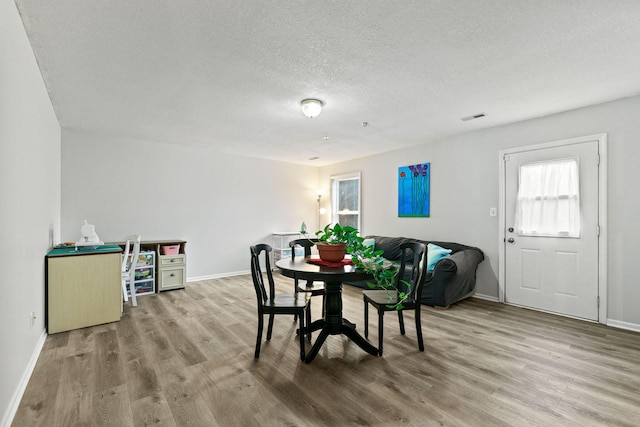 dining area featuring baseboards, a textured ceiling, visible vents, and wood finished floors