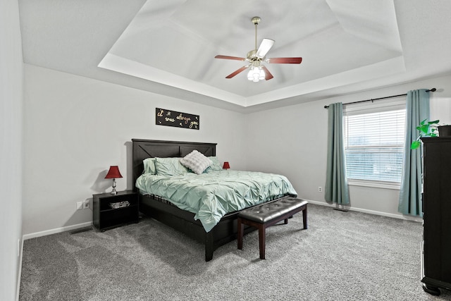 carpeted bedroom featuring a tray ceiling, ceiling fan, and baseboards