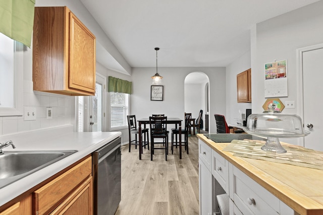 kitchen featuring arched walkways, light wood finished floors, wooden counters, stainless steel dishwasher, and a sink