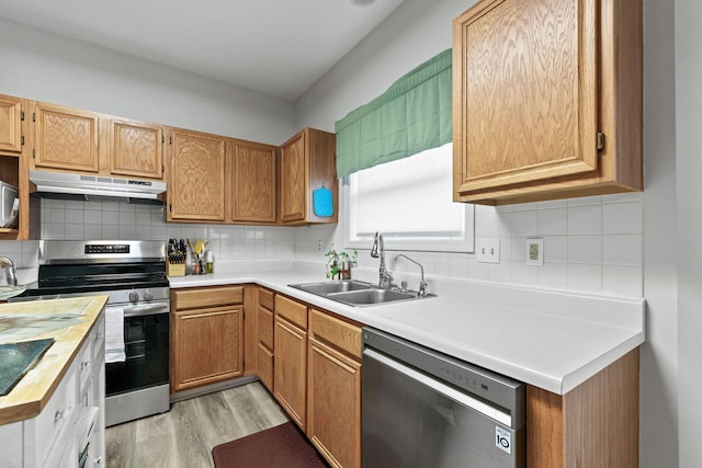 kitchen featuring light wood-style flooring, under cabinet range hood, stainless steel appliances, a sink, and tasteful backsplash