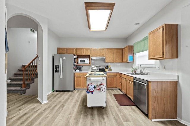 kitchen with light wood finished floors, decorative backsplash, stainless steel appliances, under cabinet range hood, and a sink