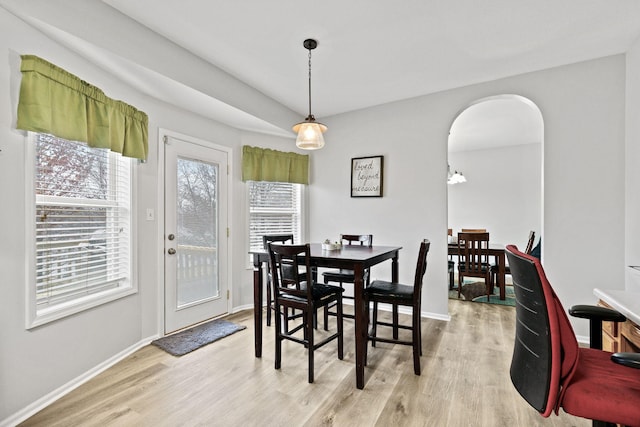 dining space featuring arched walkways, light wood-type flooring, a wealth of natural light, and baseboards