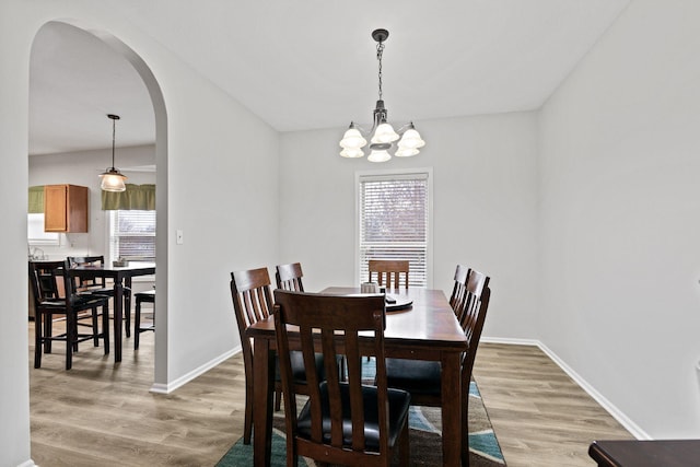 dining space with a chandelier, arched walkways, light wood-style flooring, and baseboards