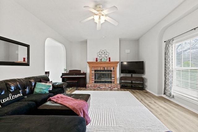 living room featuring arched walkways, ceiling fan, a fireplace, wood finished floors, and baseboards