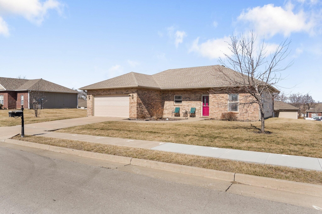 single story home with a shingled roof, concrete driveway, an attached garage, a front yard, and brick siding