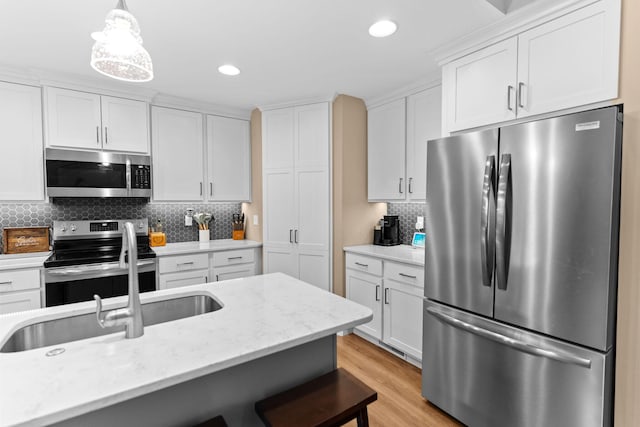 kitchen featuring tasteful backsplash, pendant lighting, light wood-type flooring, appliances with stainless steel finishes, and white cabinets