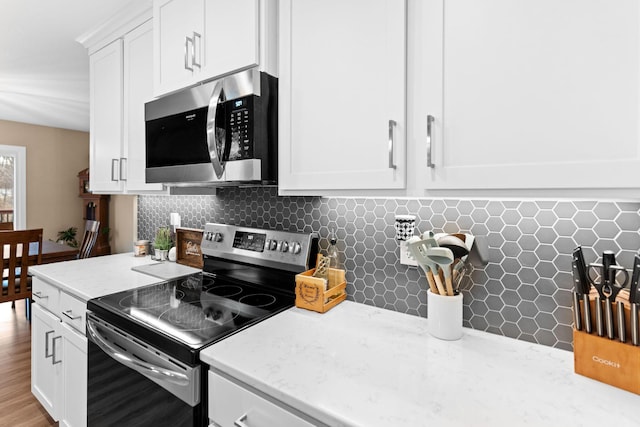 kitchen featuring backsplash, appliances with stainless steel finishes, white cabinetry, and light stone countertops