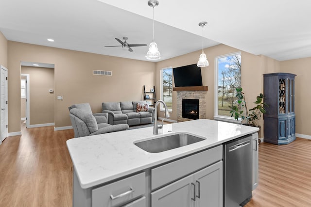 kitchen with visible vents, an island with sink, a sink, dishwasher, and open floor plan