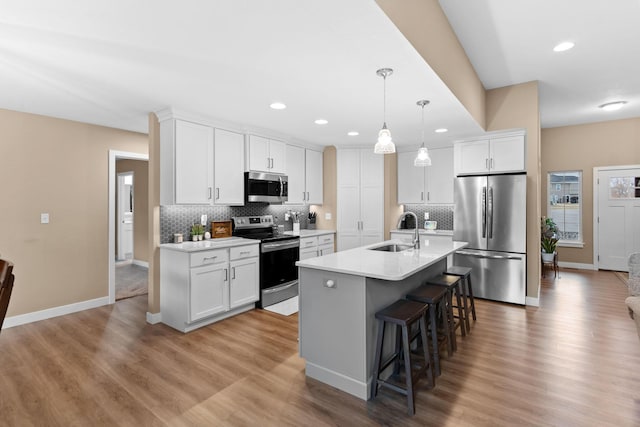 kitchen with a sink, decorative backsplash, light countertops, appliances with stainless steel finishes, and a kitchen bar