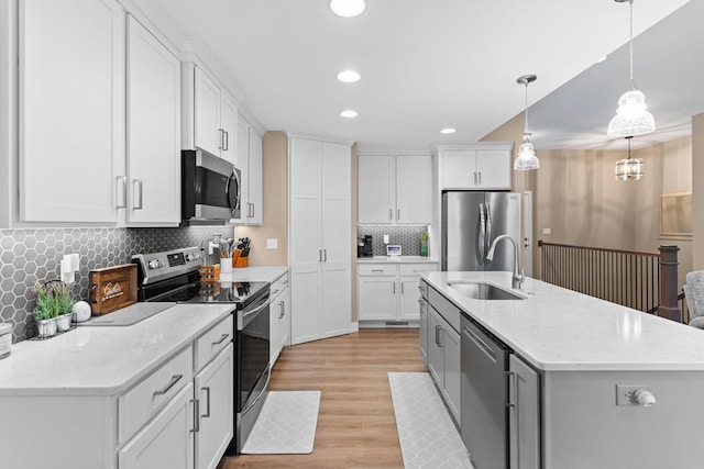 kitchen featuring an island with sink, a sink, white cabinetry, stainless steel appliances, and light wood-style floors