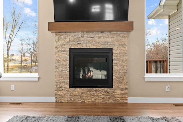 details with a glass covered fireplace, wood finished floors, visible vents, and baseboards