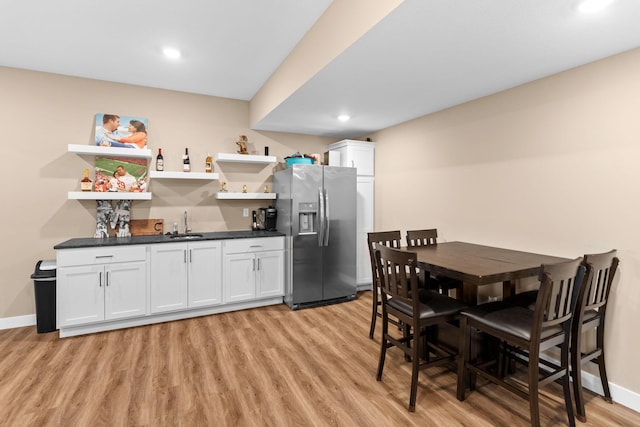 kitchen with open shelves, dark countertops, stainless steel fridge, light wood finished floors, and baseboards