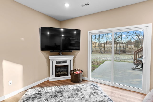 living area featuring visible vents, wood finished floors, baseboards, and a glass covered fireplace