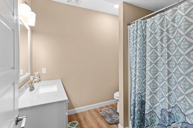 bathroom featuring baseboards, toilet, a shower with shower curtain, wood finished floors, and vanity