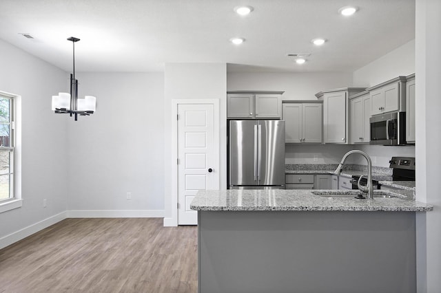 kitchen featuring light stone countertops, appliances with stainless steel finishes, gray cabinets, and a sink